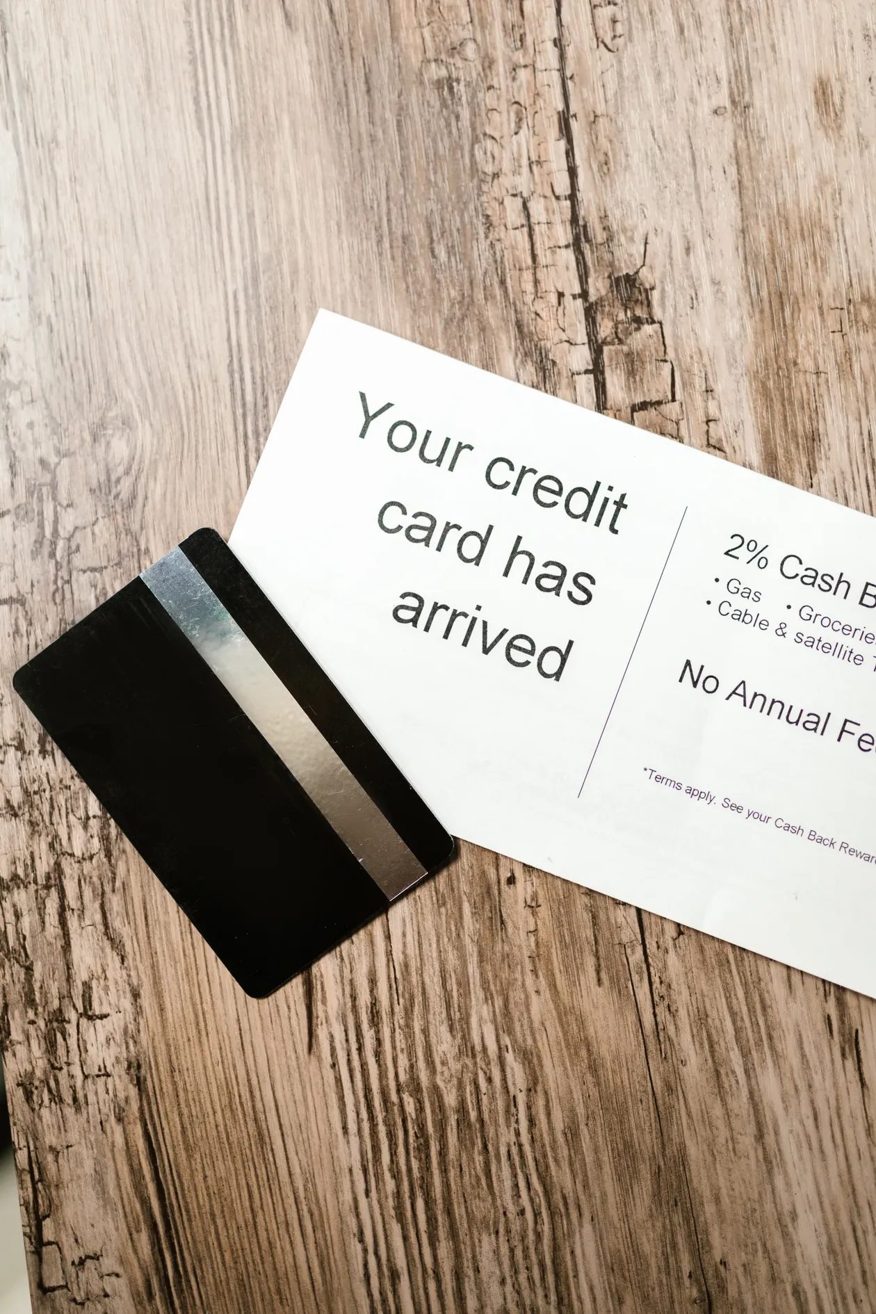 A new black credit card lying next to its welcome letter on a wooden table