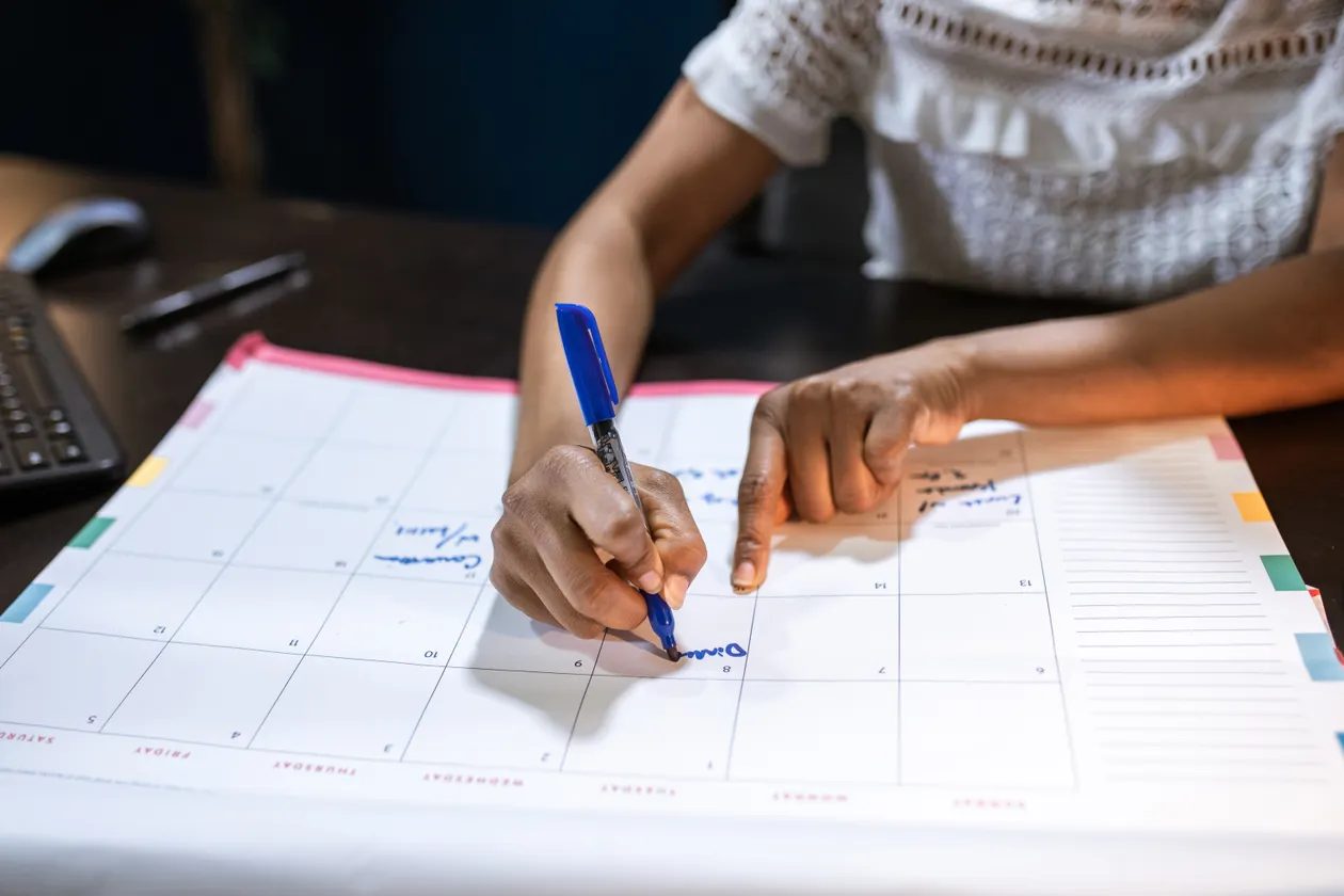 A person writing annual plans into a large paper planner with a blue pen