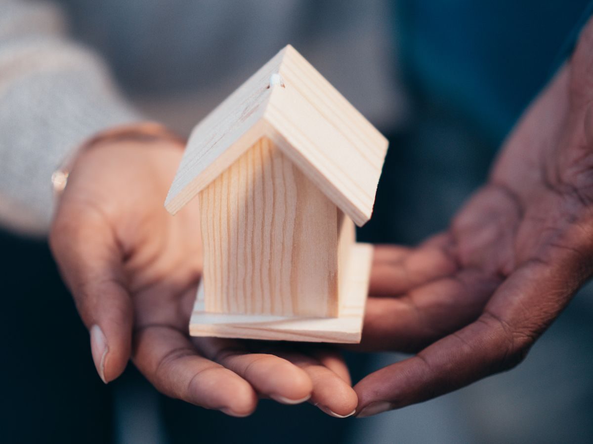 Two hands holding a small wooden model house